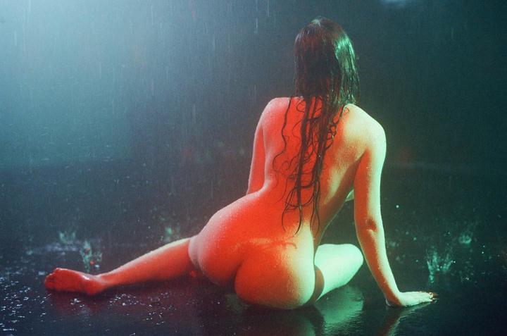 A woman sits on a wet surface with her back to the viewer, illuminated by red and green light.