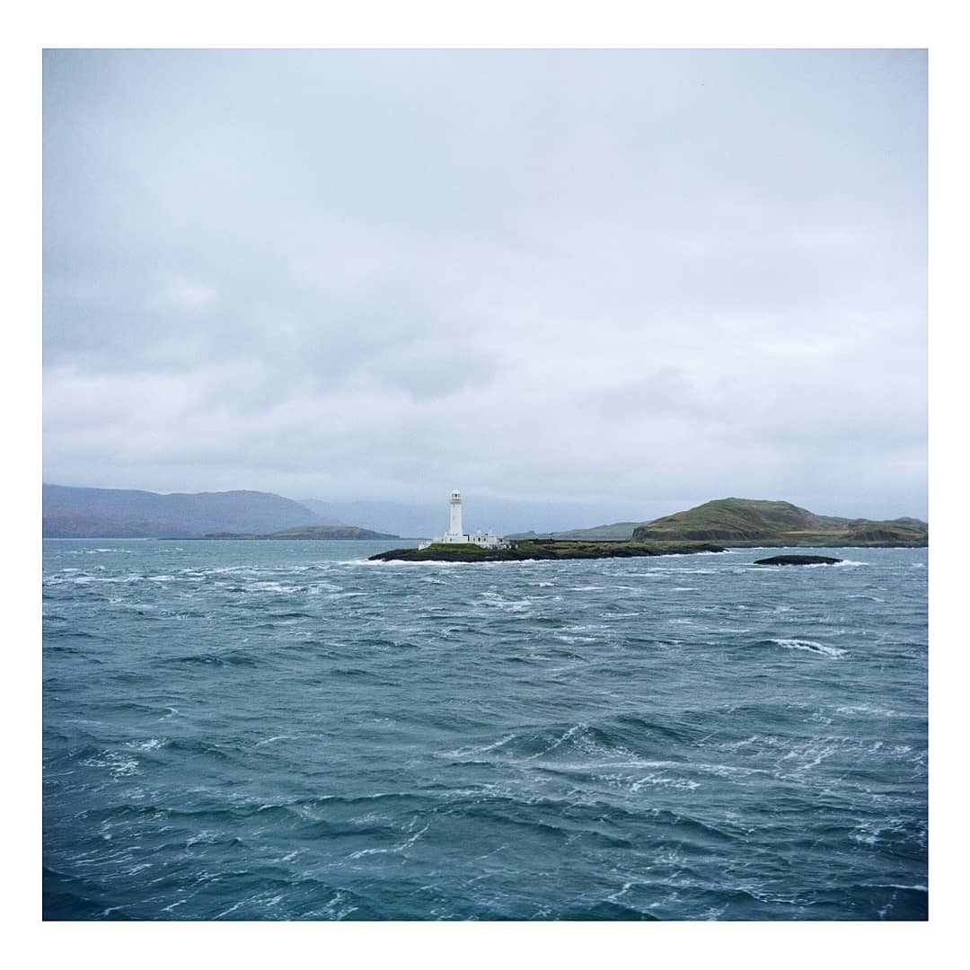 A white lighthouse stands on a small island in choppy water under a cloudy sky.