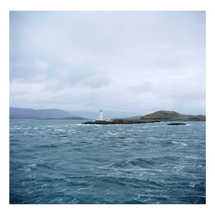 A white lighthouse stands on a small island in choppy water under a cloudy sky.