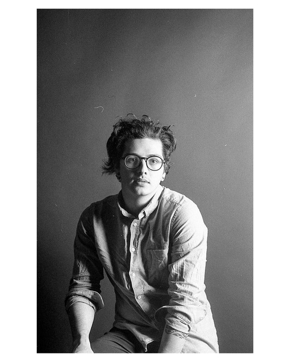 A man with glasses and curly hair sits for a portrait.
