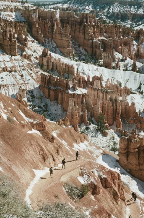 A group of people hike on a snowy trail through a canyon with towering rock formations.