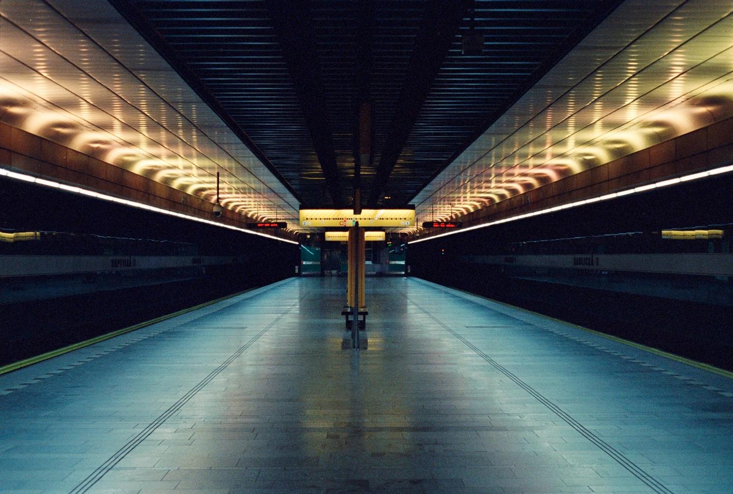 A long exposure shows an empty subway platform with illuminated ceilings and a central support column.