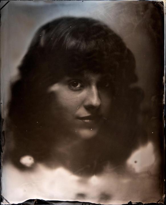 A woman with dark, curly hair looks directly at the viewer in a headshot.