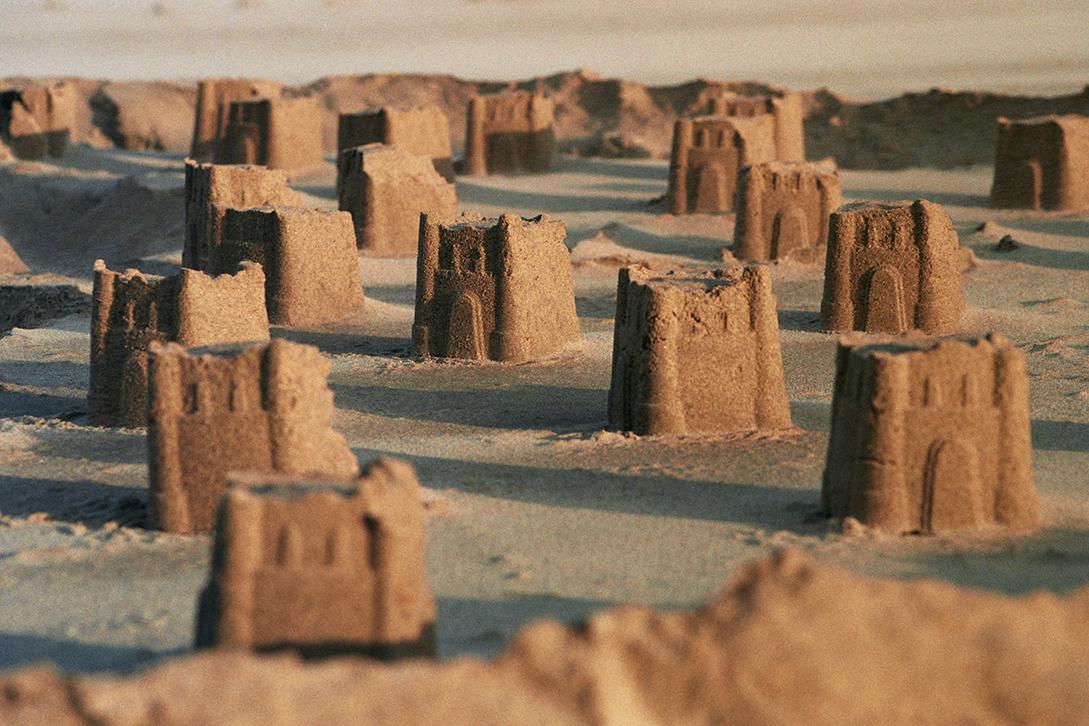 Many small sandcastles are arranged in rows on a sandy beach.