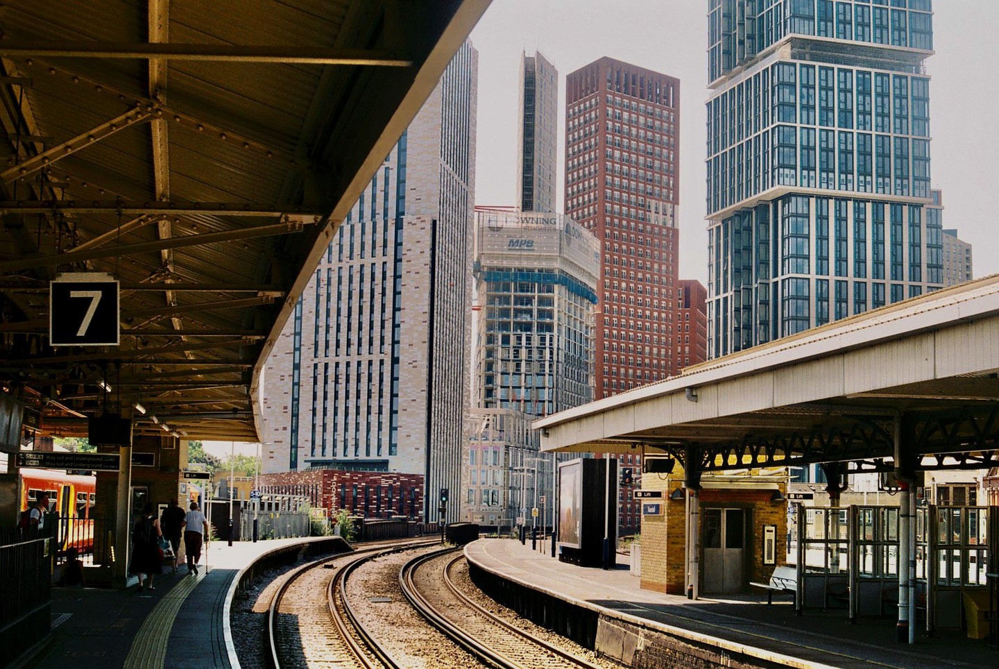 A train station platform with tracks curving to the right is surrounded by tall buildings.
