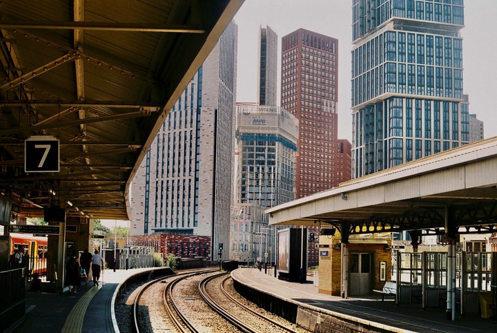 A train station platform with tracks curving to the right is surrounded by tall buildings.
