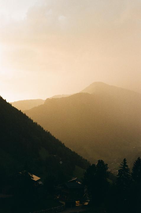 A hazy mountain landscape shows a valley with houses and trees in the foreground.