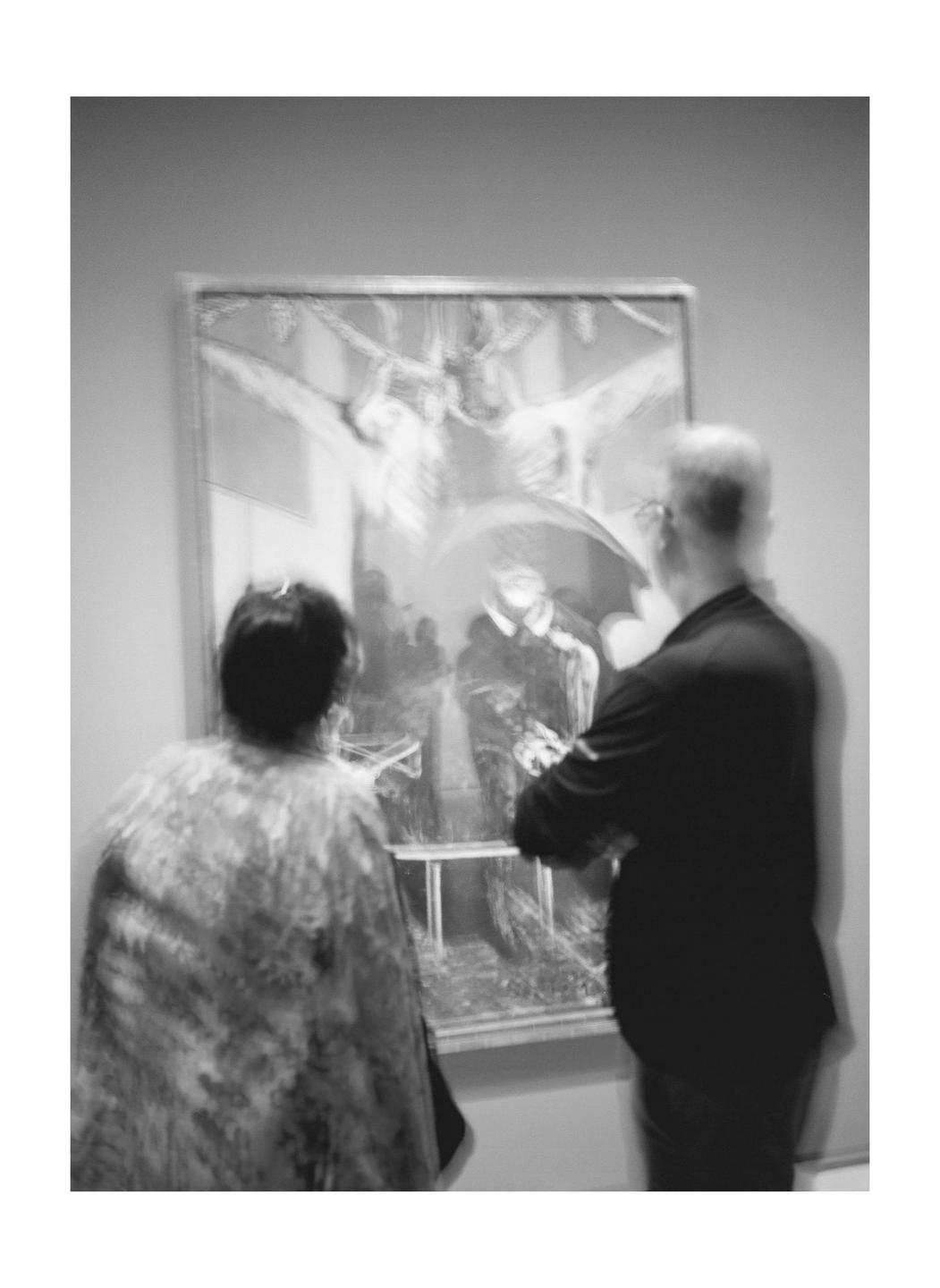A man and a woman stand in front of a painting in a museum.