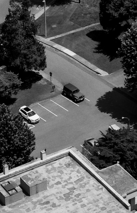 Two cars are parked on a street with three empty parking spaces between them, viewed from above.