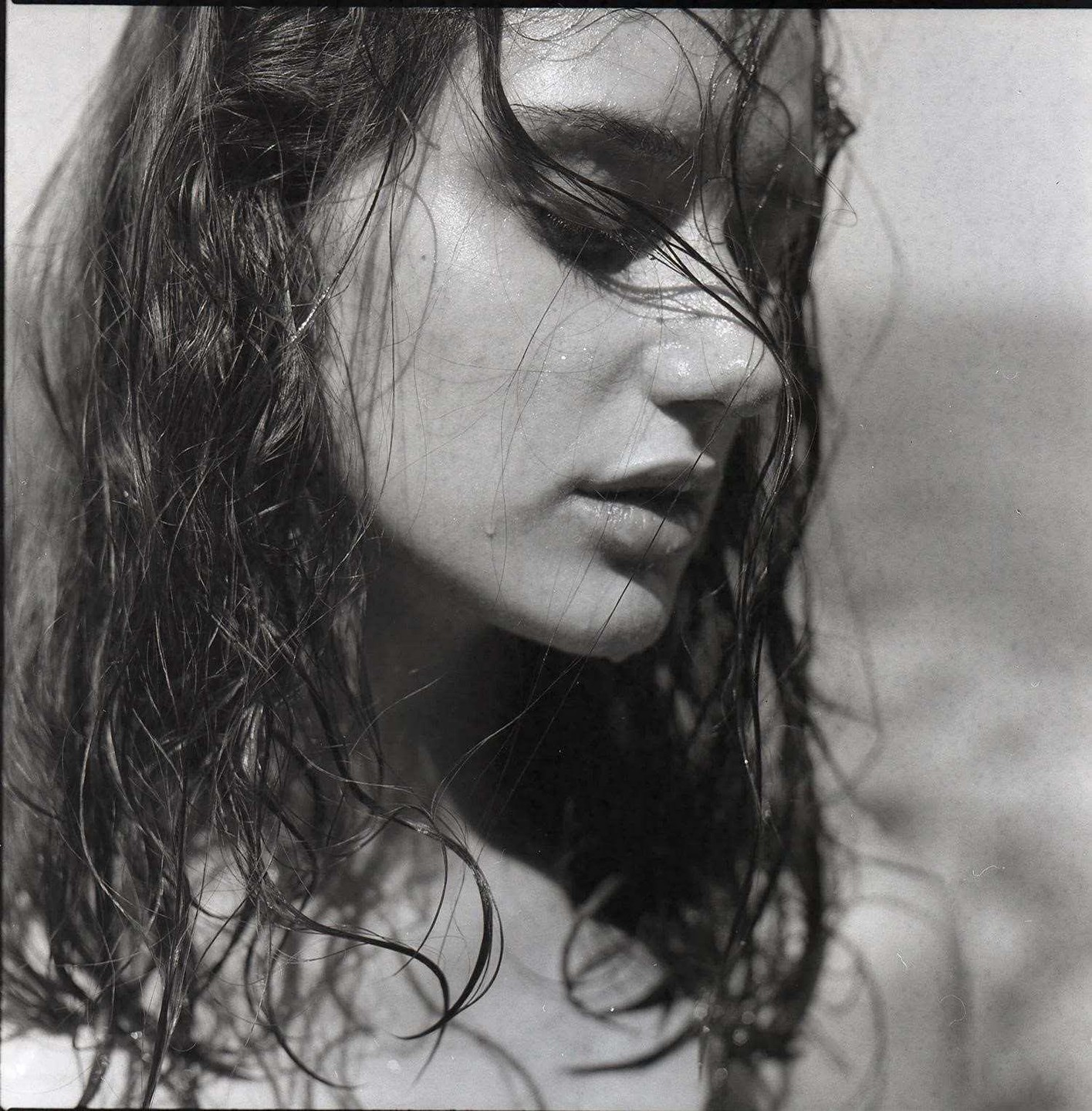A woman with wet hair and water drops on her face looks down.