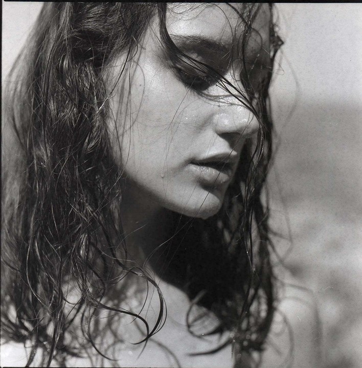 A woman with wet hair and water drops on her face looks down.