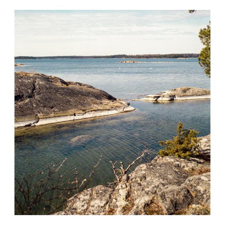 A body of water with several rocky islands and a distant tree line under a cloudy sky.