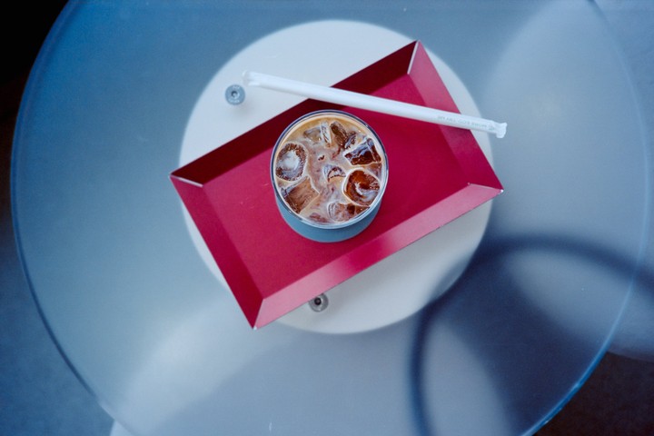 An iced coffee with a straw sits on a red tray on a glass table.