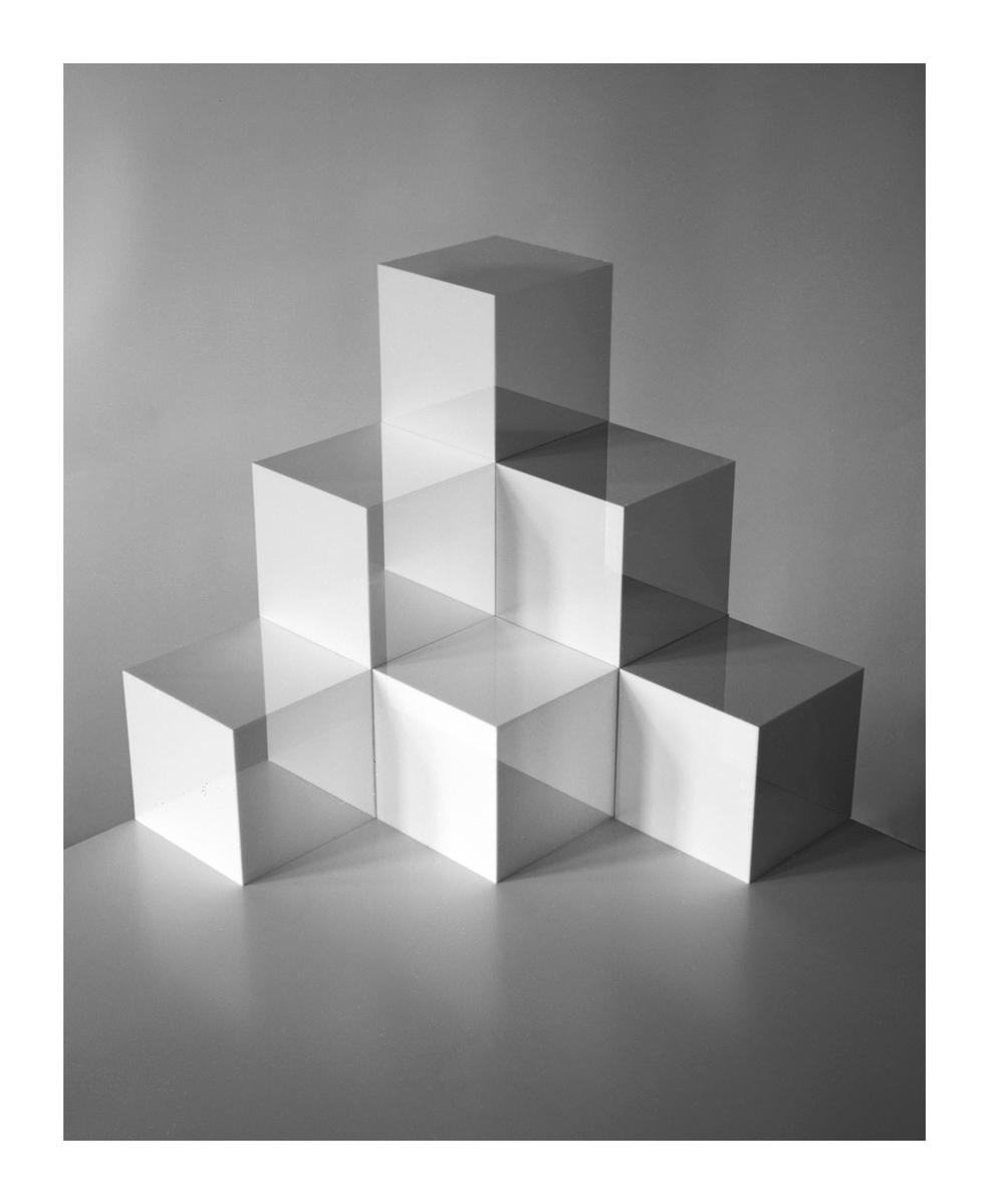 A still life shows a stack of white cubes with shadows on a gray background.