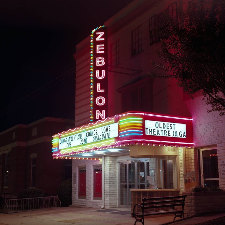 The Zebulon Theatre marquee is lit up at night with neon lights and a message congratulating a graduate.