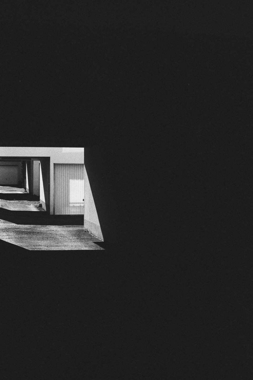 Sunlight illuminates a garage door and the ground in a black and white image with a large dark area.