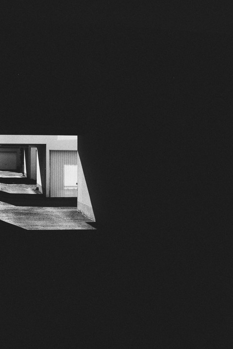 Sunlight illuminates a garage door and the ground in a black and white image with a large dark area.