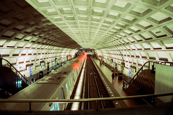 A subway train is stopped at a station with a vaulted, coffered ceiling.