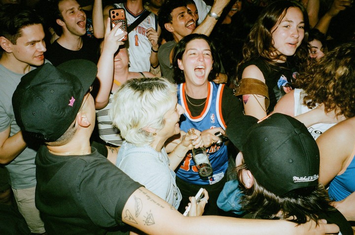 A crowd of people celebrate, with one woman in a basketball jersey laughing with her mouth open.