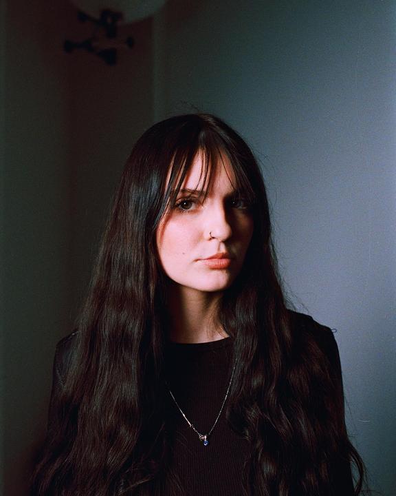 A woman with long dark hair and bangs looks directly at the viewer.