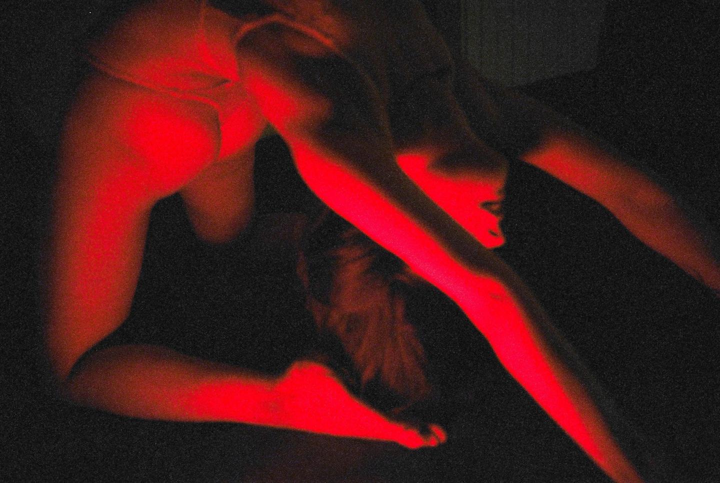A woman is illuminated by red light while posing on her hands and knees.