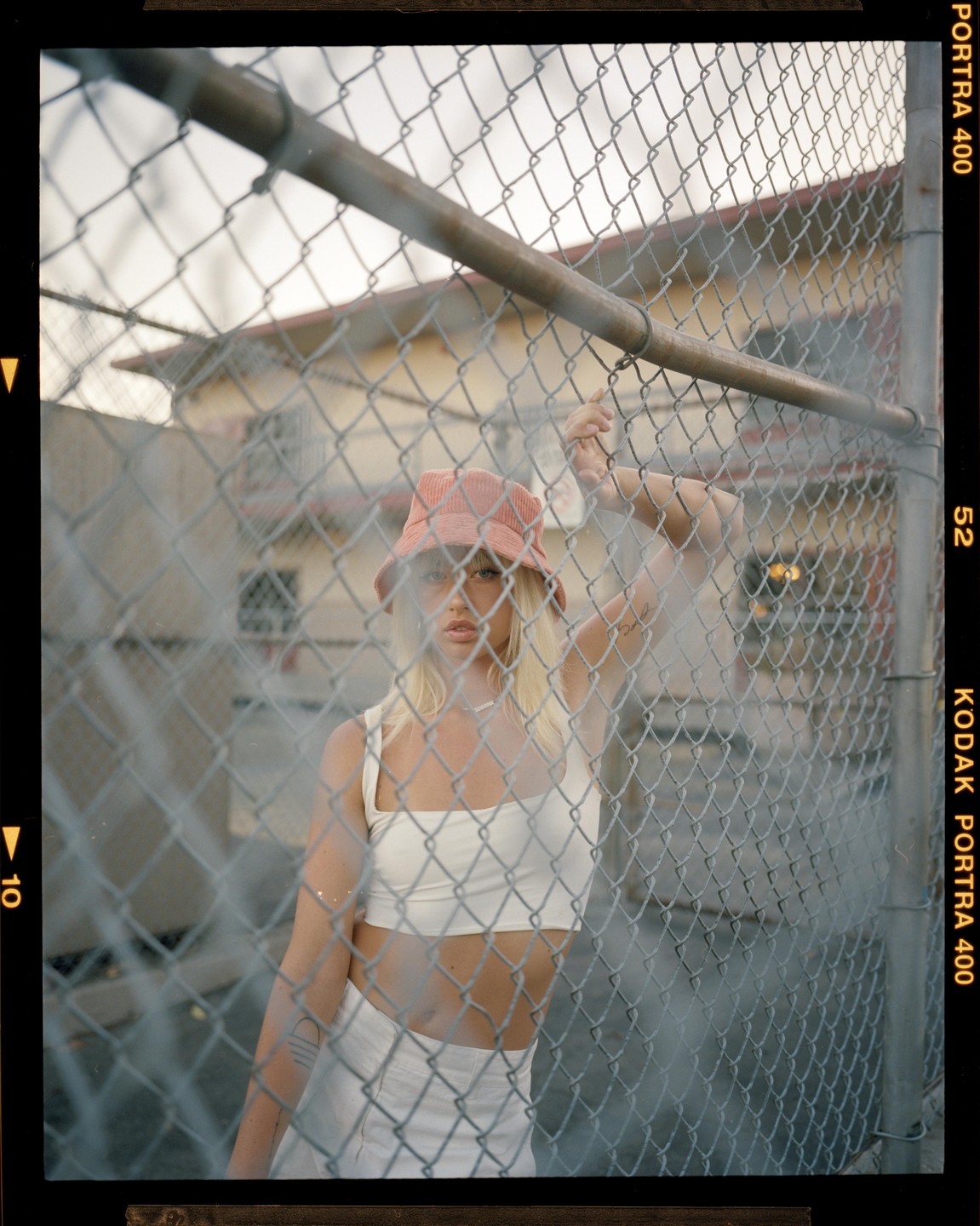 A woman in a bucket hat and crop top stands behind a chain link fence.