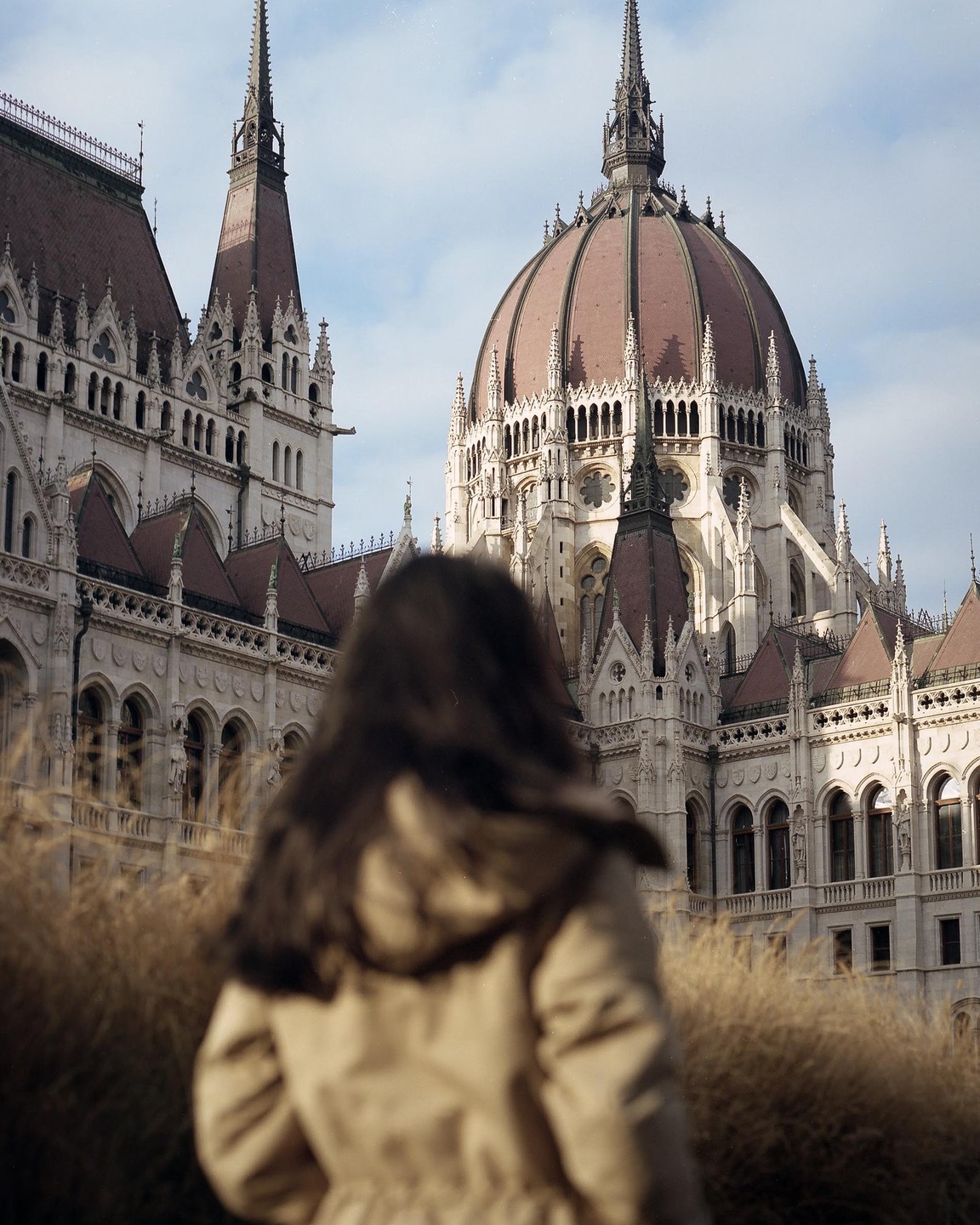A woman stands in front of a large ornate building with a domed roof.