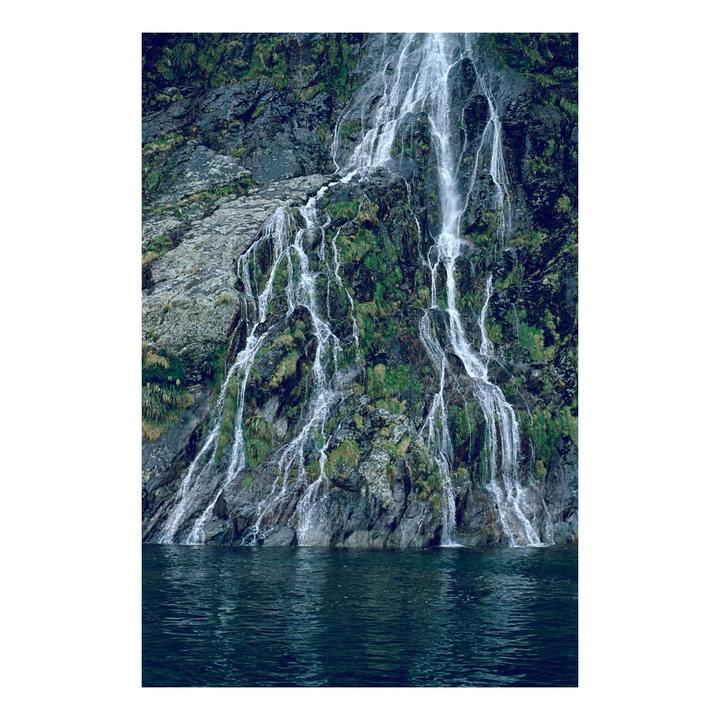 A waterfall cascades down a mossy rock face into a body of water.