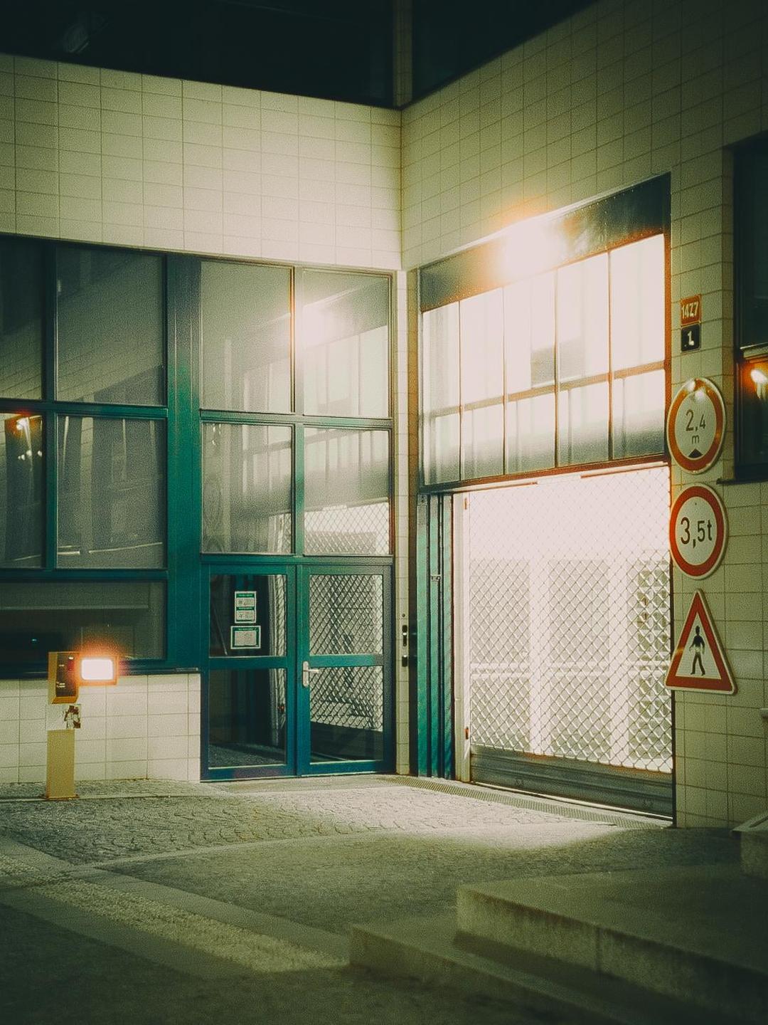 A building with large windows and a garage door is illuminated by artificial light at night.