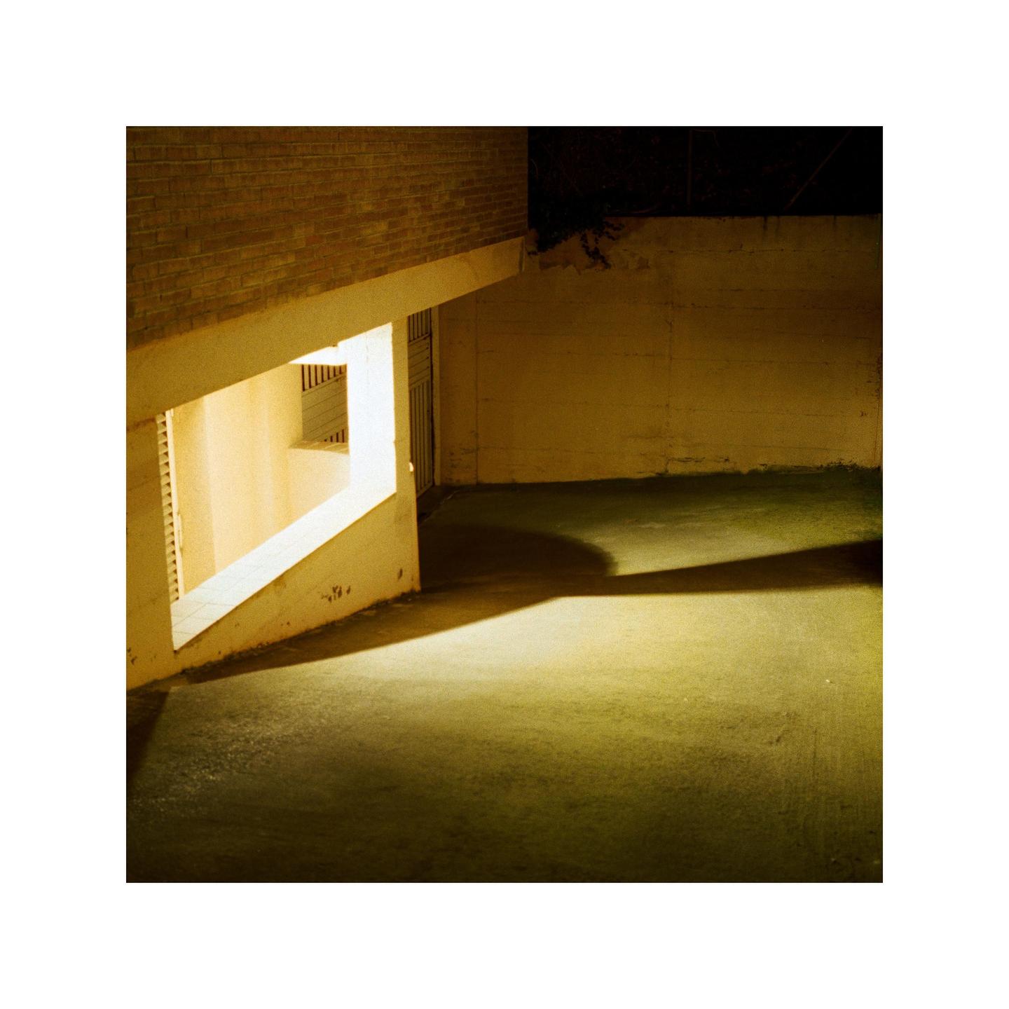 A brightly lit window casts a long shadow across a concrete floor at night.