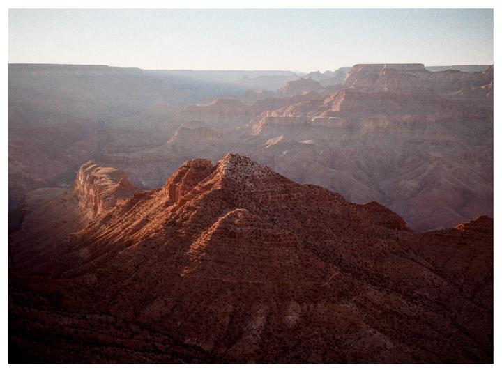 A vast canyon landscape is illuminated by the setting sun, casting long shadows across the rugged terrain.