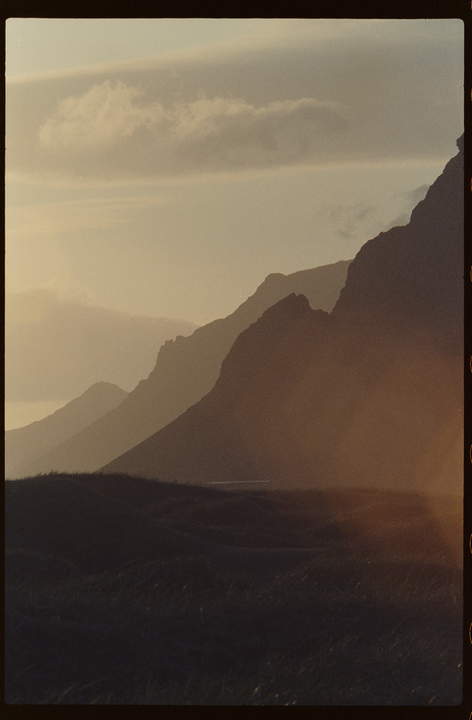 A golden hour landscape shows layers of mountains and hills under a hazy sky.