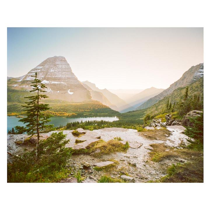 A mountain lake is surrounded by a forest and mountains under a hazy sky.