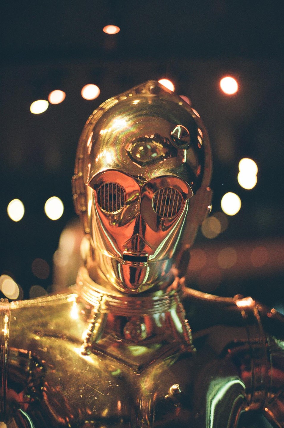 A golden robot with glowing eyes is shown from the chest up against a dark background with bokeh lights.