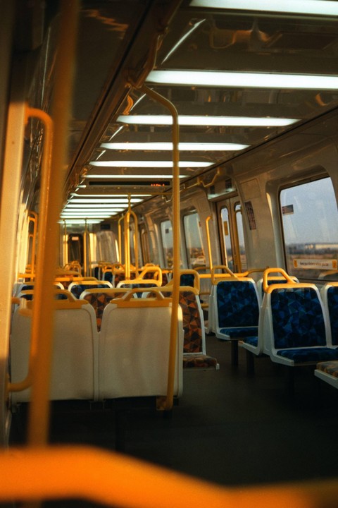 The interior of an empty train car is illuminated by warm light from the windows and bright overhead lights.