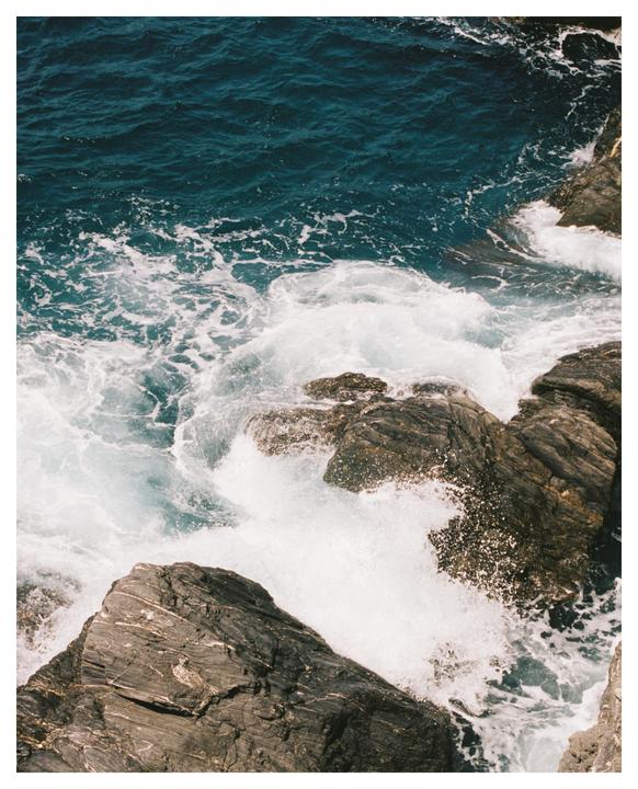 Waves crash against dark rocks along a coastline.