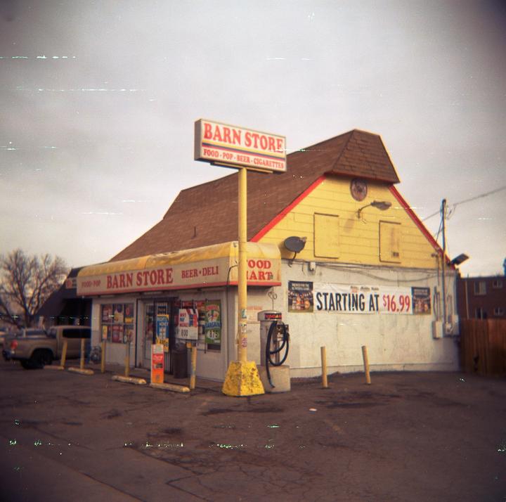 A yellow and brown convenience store with a large sign stands under a cloudy sky.