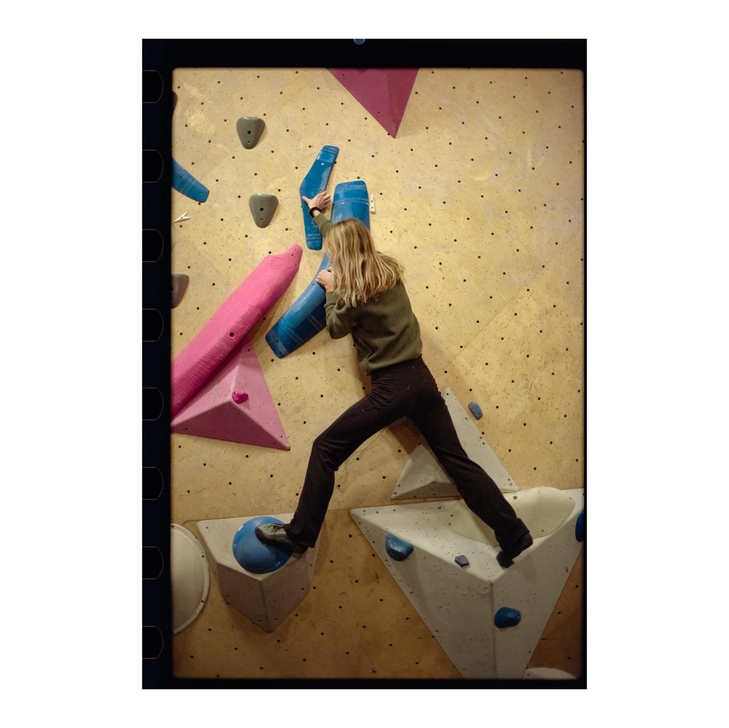 A woman climbs an indoor rock wall with colorful holds.