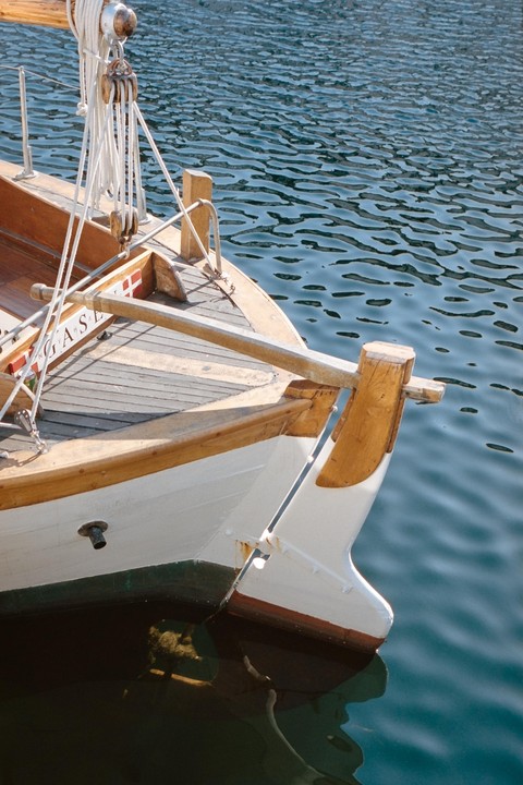 A wooden sailboat with white and green hull is moored in blue water.