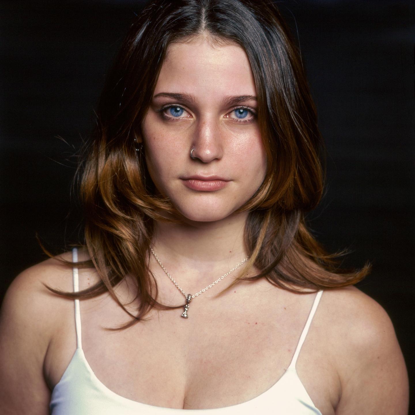 A young woman with blue eyes and brown hair looks directly at the viewer.