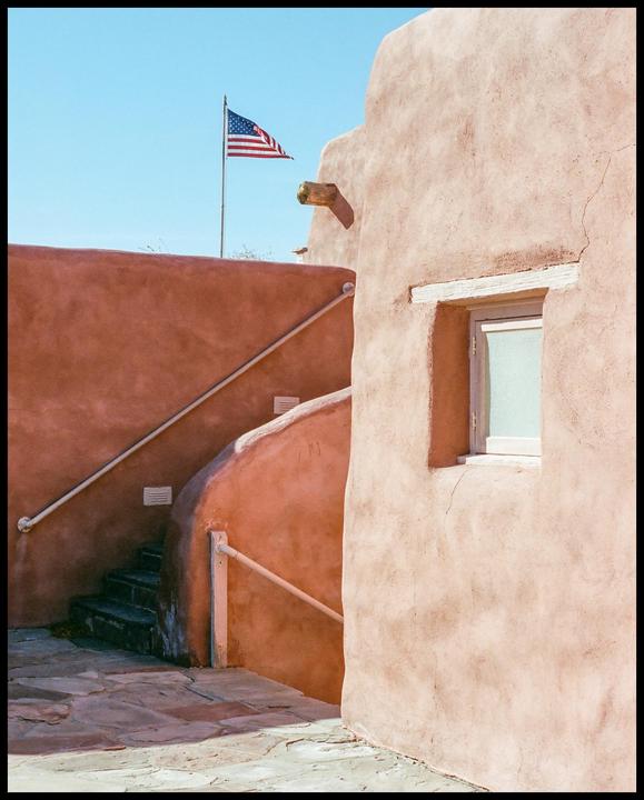 An American flag flies above a building with adobe walls and a staircase.