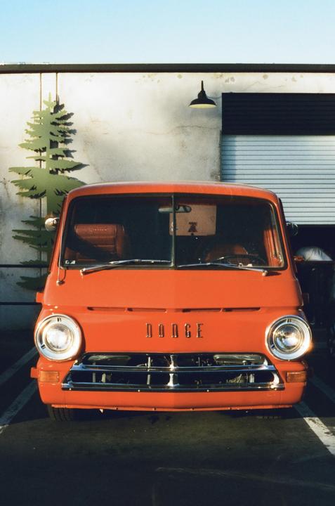 An orange Dodge van is parked in front of a building with a painted tree.