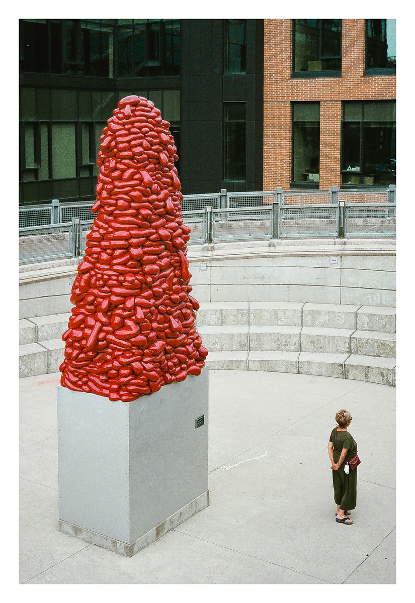 A woman stands in front of a large red sculpture in an urban setting.