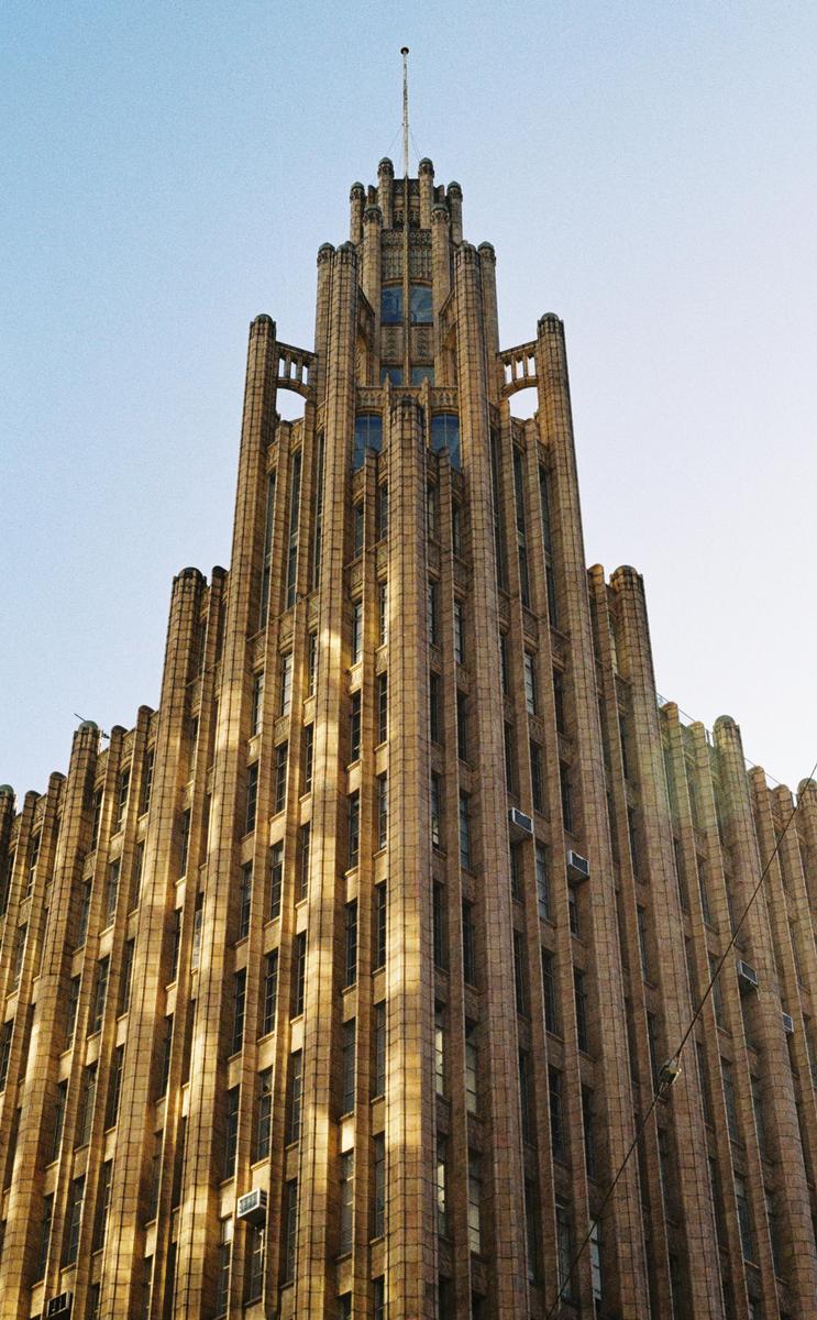A tall, ornate building with many windows and a spire on top stands against a clear sky.