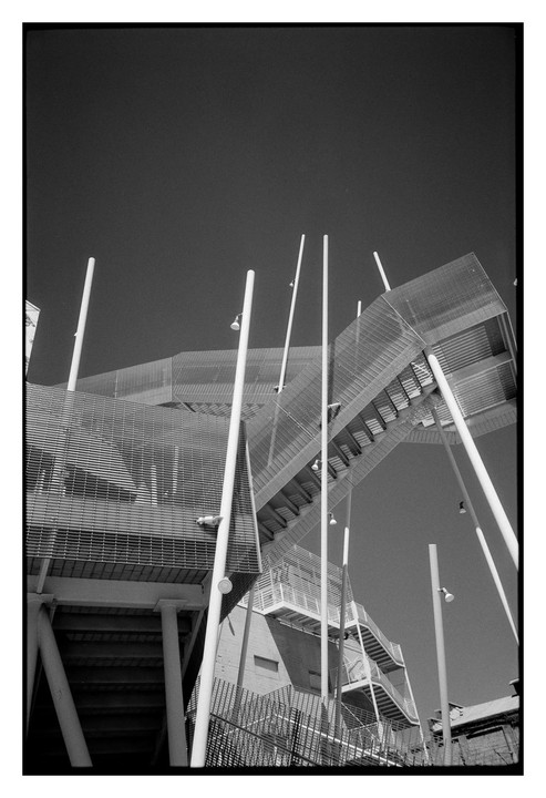 A low-angle view shows a modern building with multiple staircases and white poles against a clear sky.