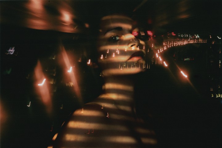 A woman's face and shoulder are illuminated by horizontal stripes of light and surrounded by blurred light trails at night.