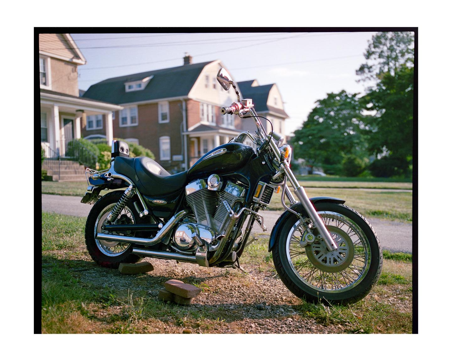 A black motorcycle is parked on a grassy area in front of houses.
