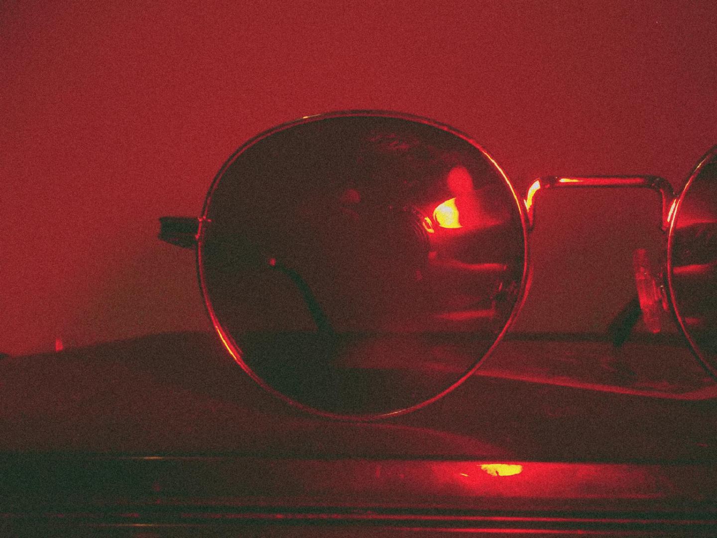 A pair of round glasses is illuminated by a red light.
