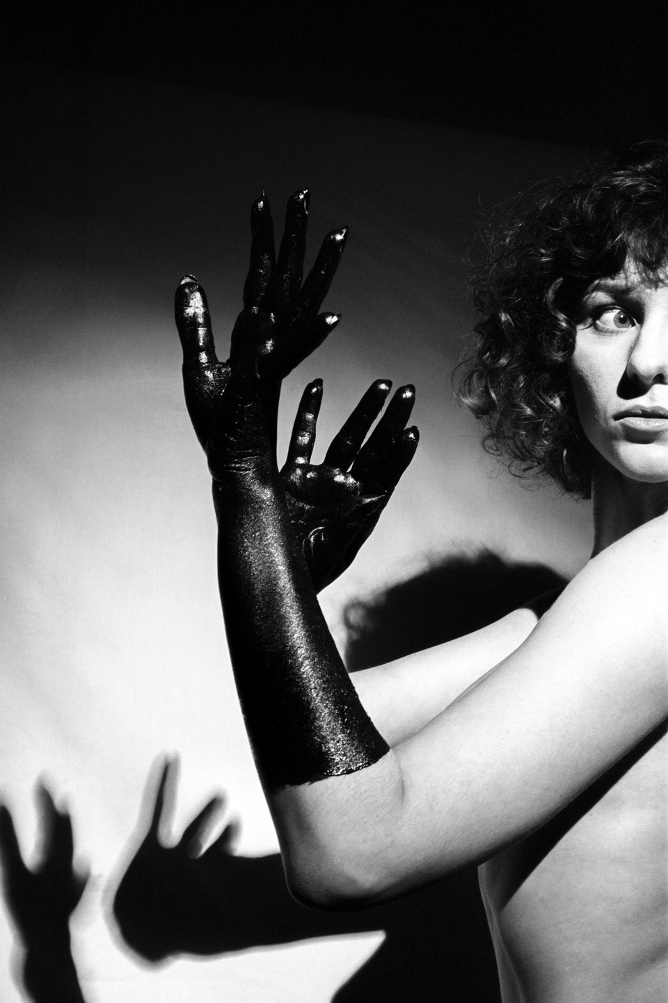A woman with black painted arms looks to the right with a surprised expression.