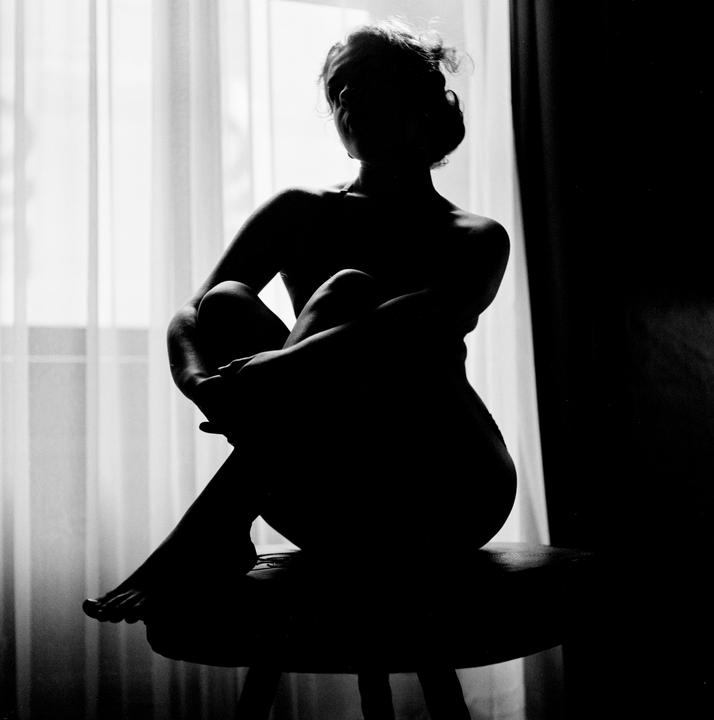 A woman is silhouetted against a window with sheer curtains.